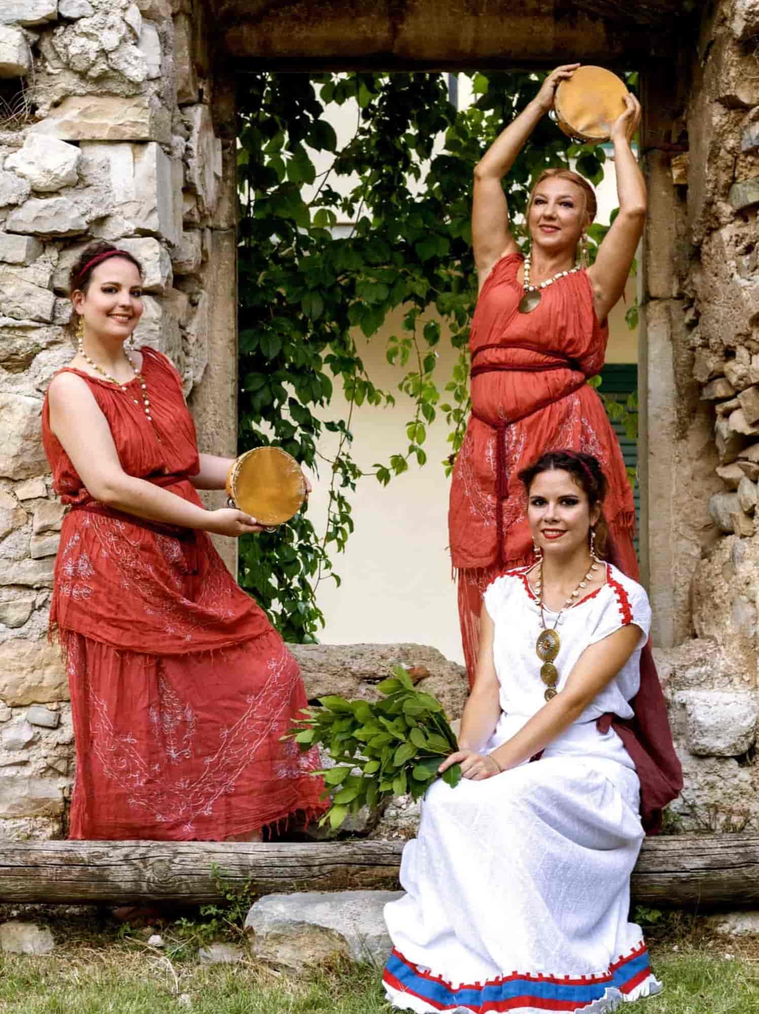 Interpreti del gruppo Venus in danze romane antiche con abiti e strumenti rituali davanti a una struttura in pietra