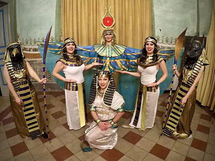 Figuranti in costumi ispirati agli Dei dell’Antico Egitto durante una performance scenica con abiti rituali e pose cerimoniali.