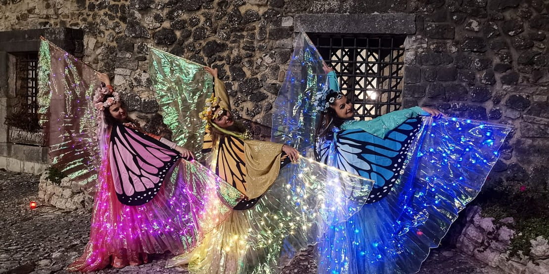 Farfalle luminose danzanti in costumi scenici con ali illuminate, ideali per feste ed eventi in ambientazione fantasy.