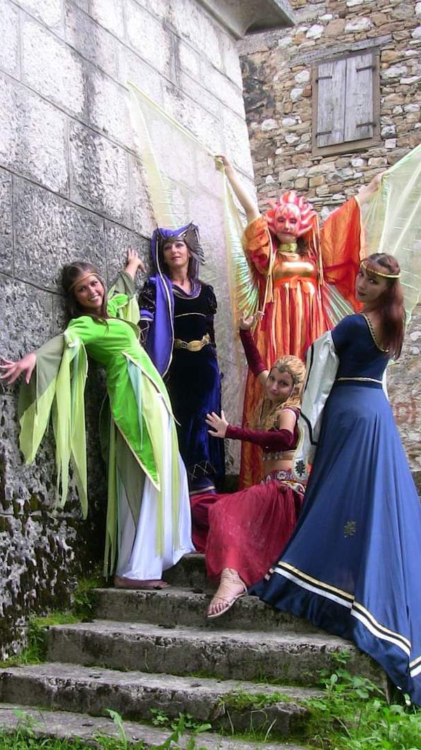 Fate, maghe e folletti in costumi fantasy durante una performance scenica su scalinata in pietra.