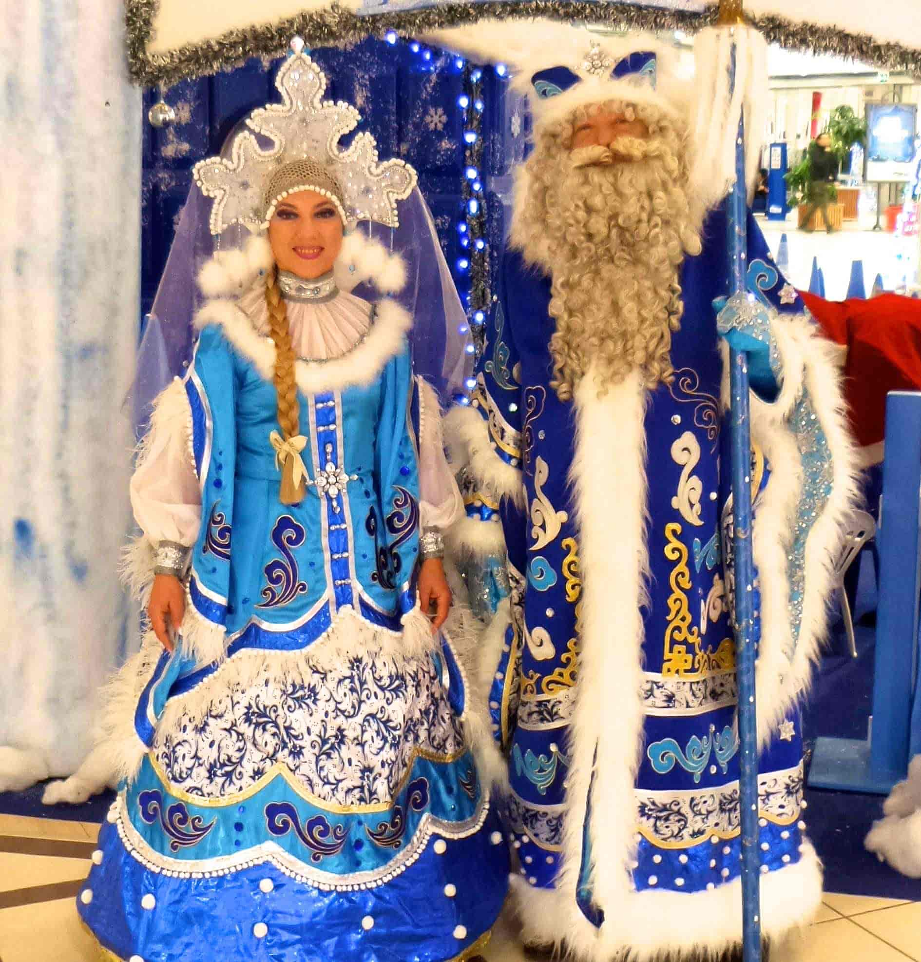 Personaggi natalizi Nonno Gelo e Nevina in costumi invernali tradizionali, con scenografia luminosa a tema festivo.