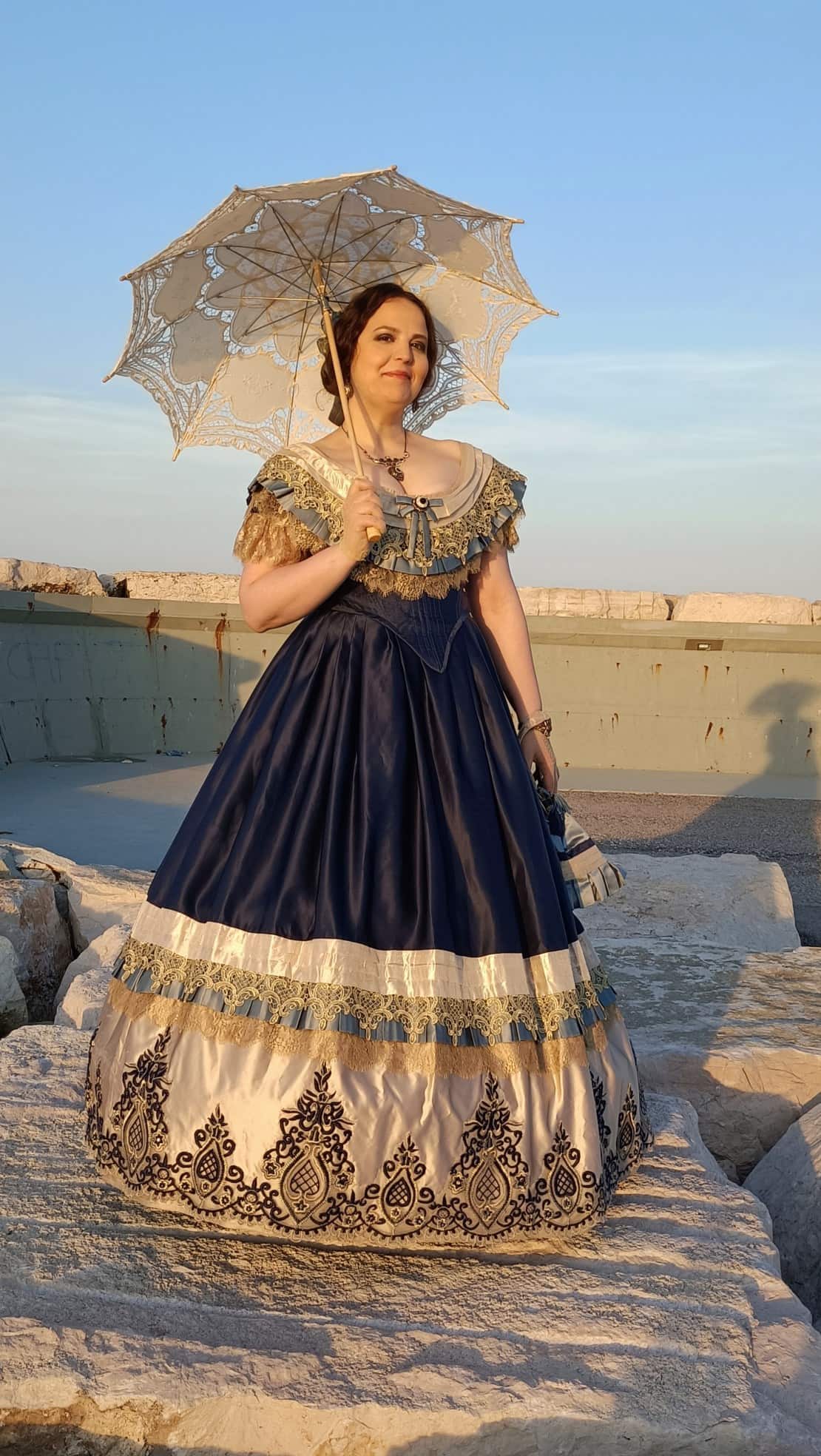 Figurante in abito storico ottocentesco con parasole durante una passeggiata culturale in ambientazione all’aperto.