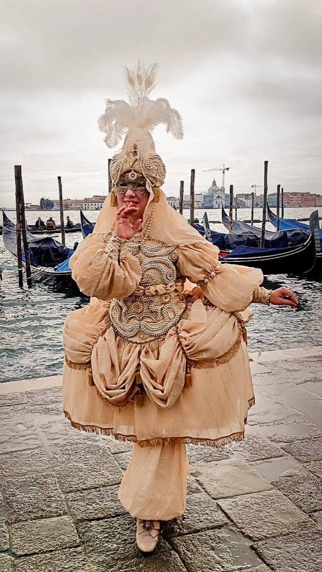 Figurante in costume elaborato del Carnevale Veneziano con maschera e abito ricamato in ambientazione lagunare.