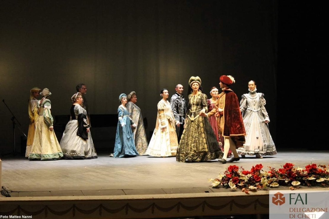 Figuranti in abiti storici rinascimentali durante una sfilata o corteo in ambientazione teatrale.