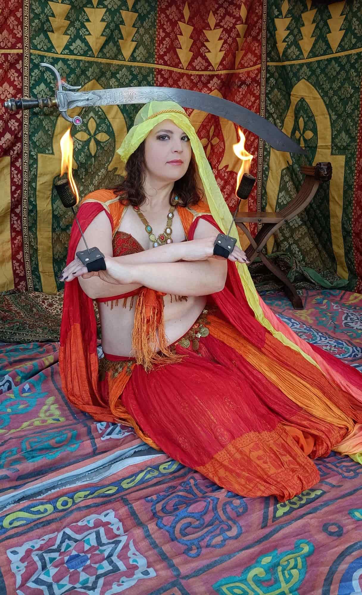 Danzatrice in costume mediorientale antico con spada, fuoco e vassoio in una performance ispirata a Salomè